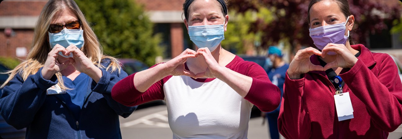 A group of people wearing face masks and making heart symbols with their hands.