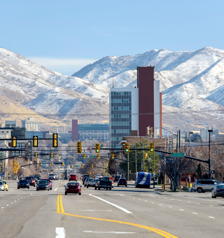 A city street with a tall building and snowy mountains in the background.