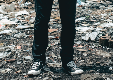 A pair of legs in jeans and shoes standing on a pile of leaves.