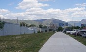 A sidewalk and parking lot with cars and buildings and mountains in the background.