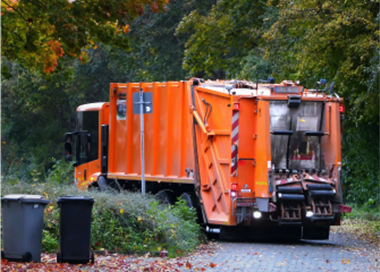 A large orange truck is parked in a wooded area.