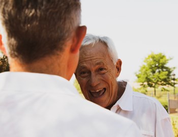 An older man smiling and speaking to a younger man. 