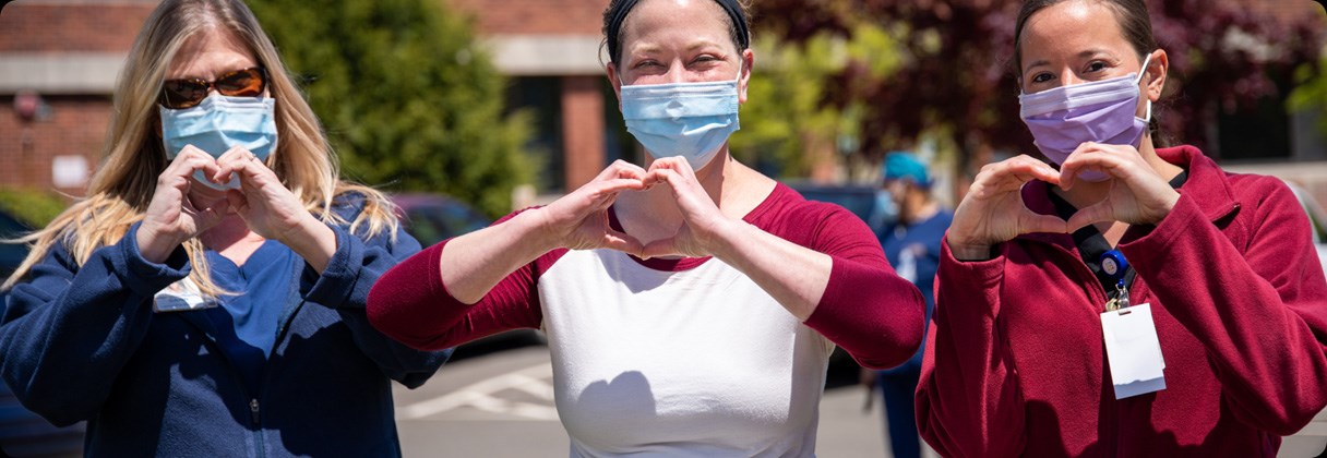 A group of people wearing face masks and making heart symbols with their hands.