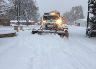 A snow plow driving through a snowy road.