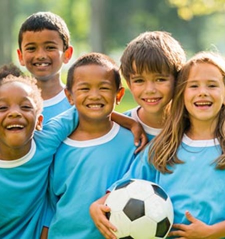 A group of smiling kids in blue shirts with a soccer ball.