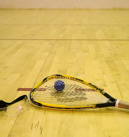 A tennis racket and a ball on a wooden floor.